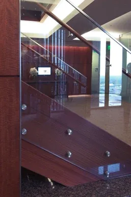 Laminated glass railing with metal mounting hardware on an interior staircase.